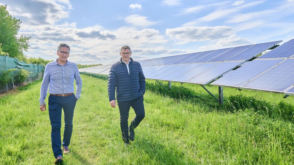 Solarpark Görgeshausen Zwei Personen gehen über eine Grünfläche entlang einer großen Photovoltaikanlage mit Solarmodulen, die sich in mehreren Reihen über das Gelände erstrecken, unter blauem Himmel mit Wolken.