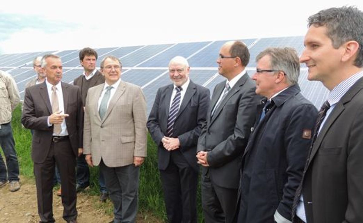 Mehrere professionell gekleidete Männer stehen vor einem Solarpark