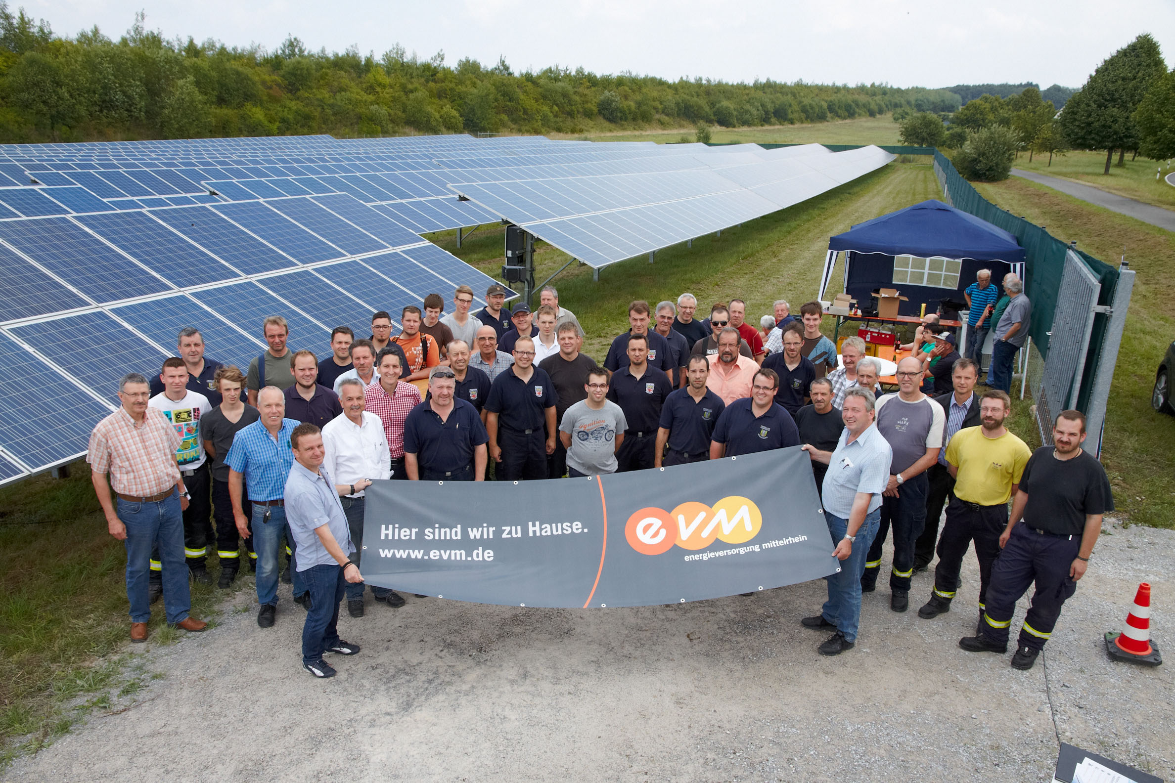 Eine Gruppe von Menschen steht vor einem Solarpark und hält einen evm-Banner