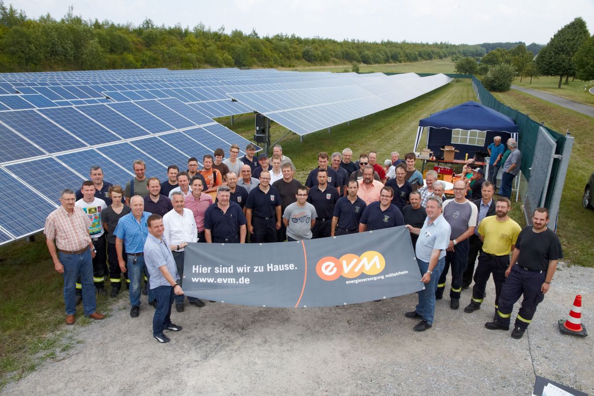 Eine Gruppe von Menschen steht vor einem Solarpark und hält einen evm-Banner