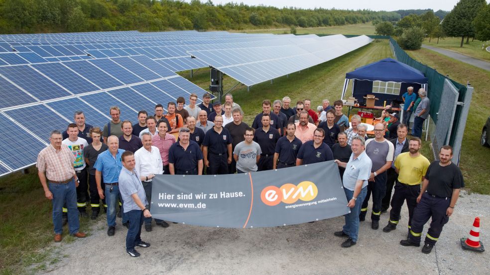 Eine Gruppe von Menschen steht vor einem Solarpark und hält einen evm-Banner
