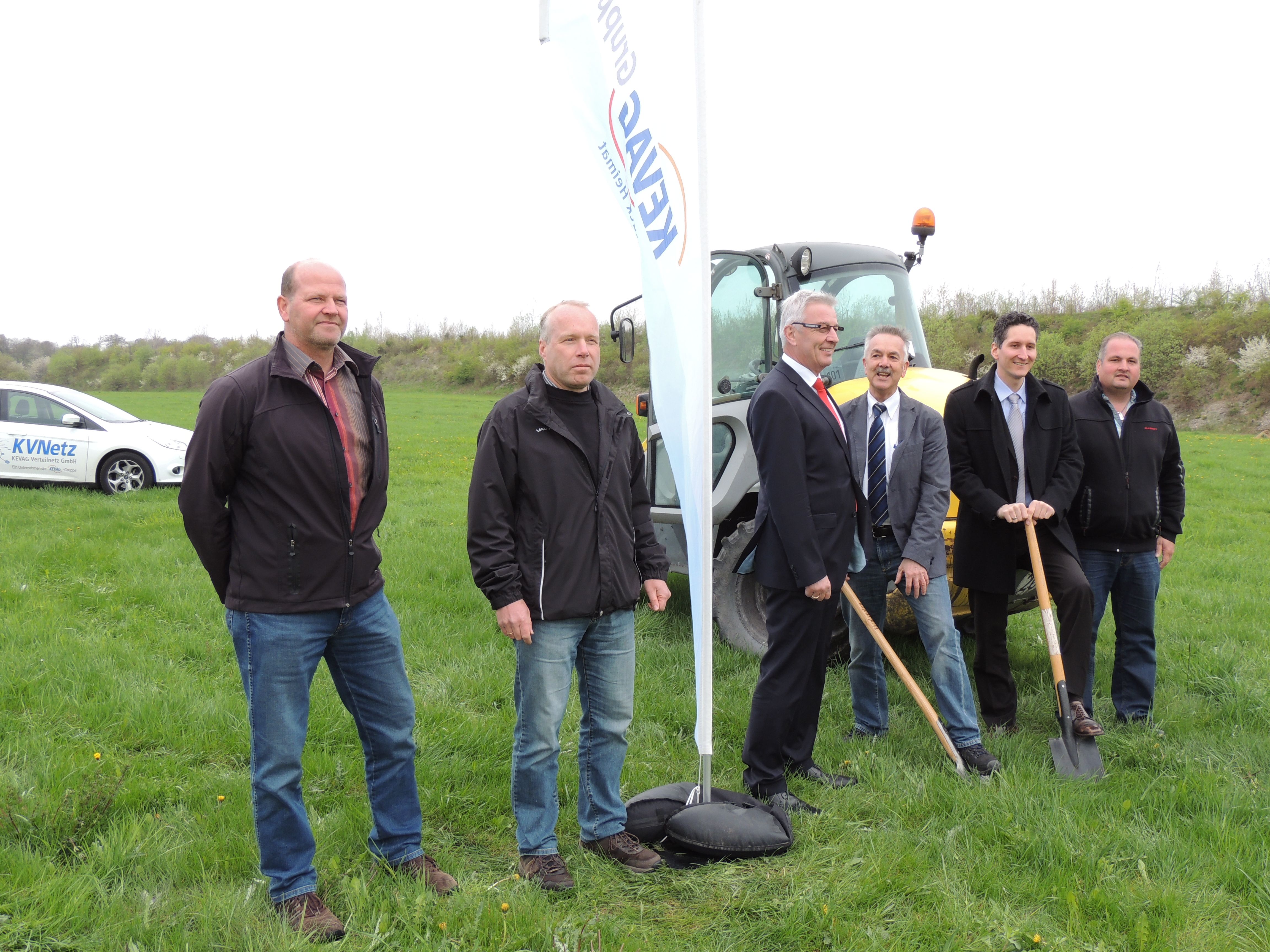 Spatenstich Solarpark Görgeshausen. Mehrere Männer stehen auf einer Wiese. Hinter ihnen steht ein Bagger. Zwei Männer halten einen Spaten.