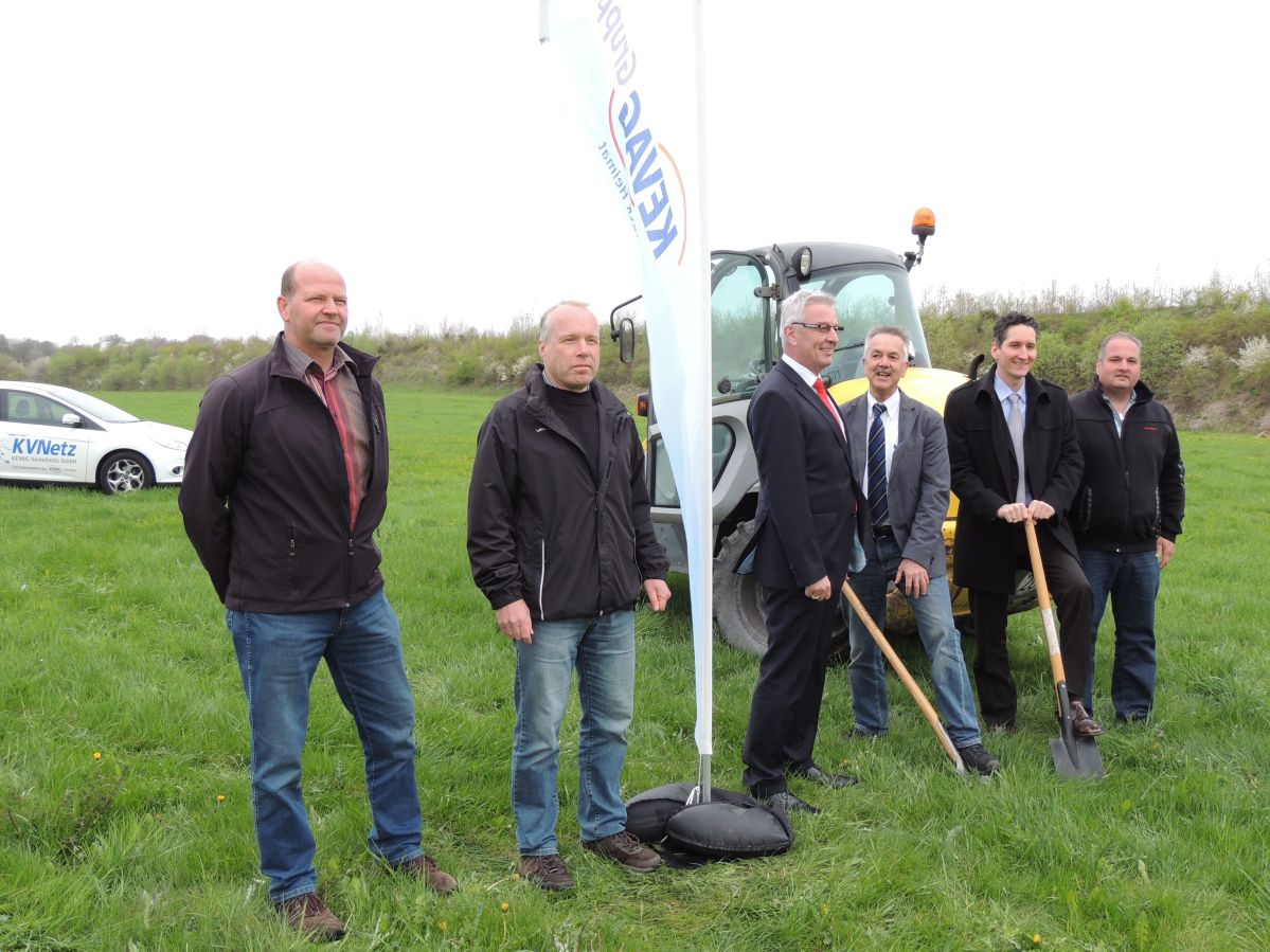 Spatenstich Solarpark Görgeshausen. Mehrere Männer stehen auf einer Wiese. Hinter ihnen steht ein Bagger. Zwei Männer halten einen Spaten.